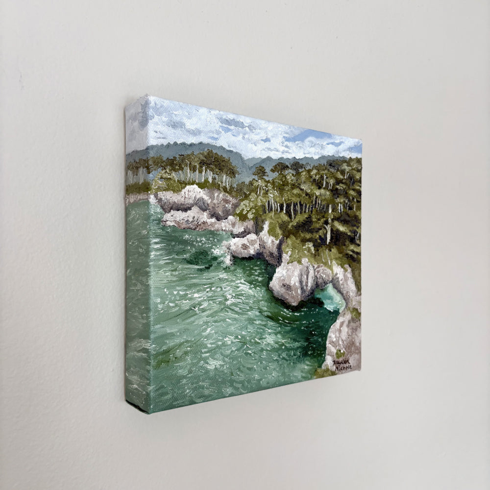 Original oil on canvas painting of a coastal landscape with trees and rocks, hanging on a white wall