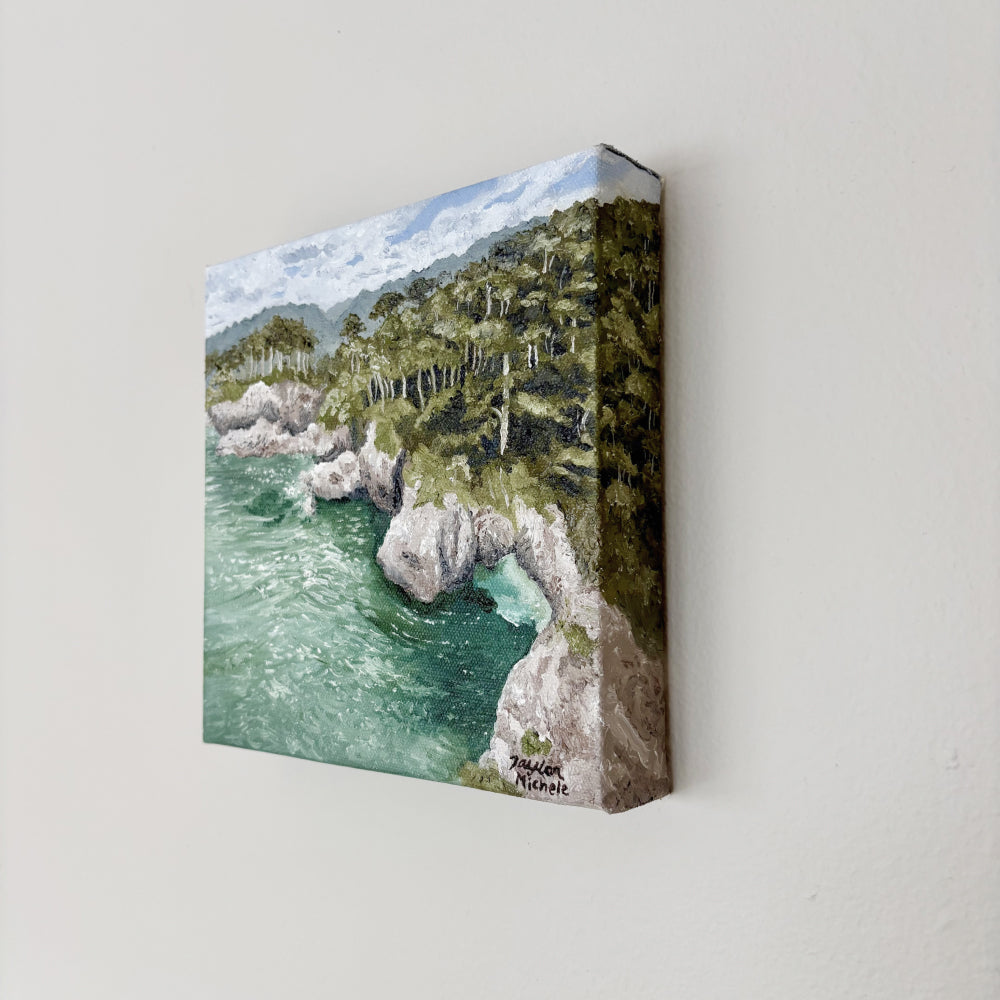 Original oil on canvas painting of a coastal landscape with trees and rocks, hanging on a white wall