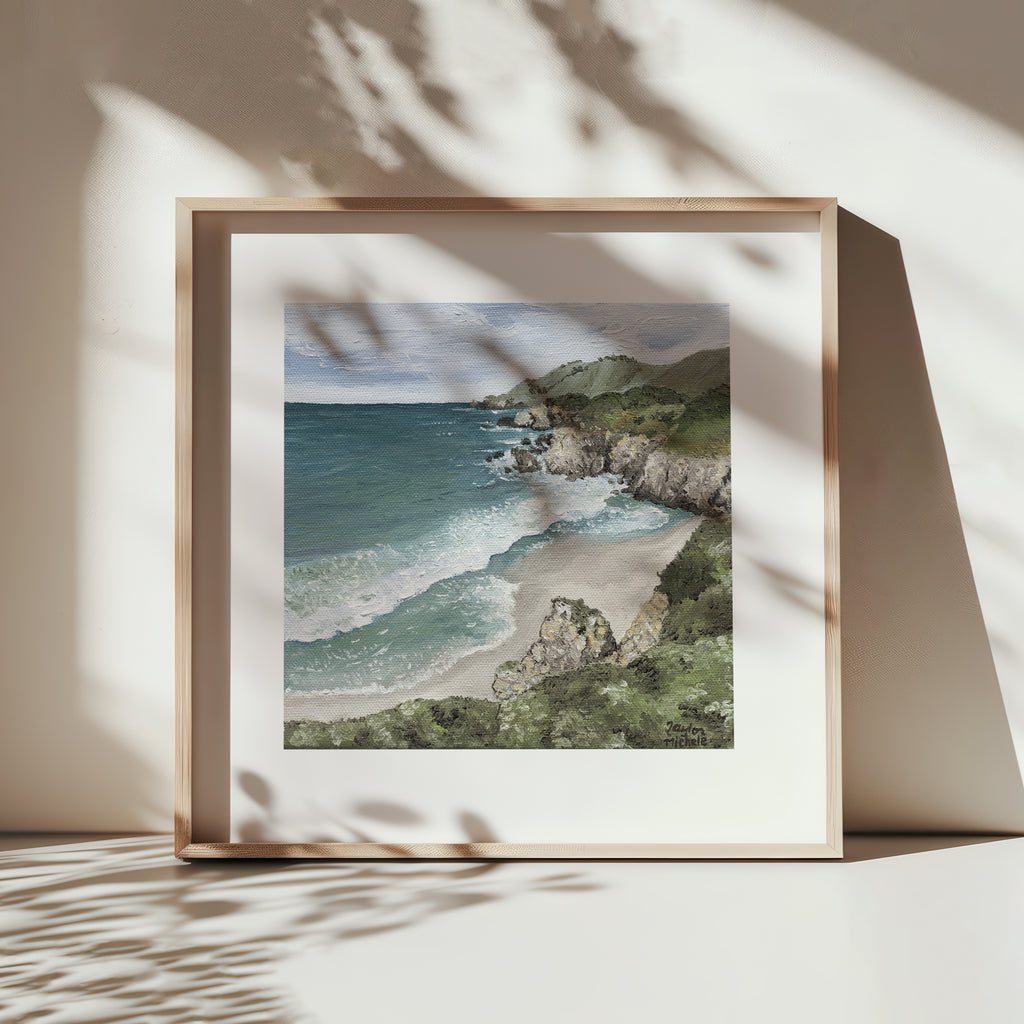 Framed artwork of a coastal landscape with a beach and ocean.