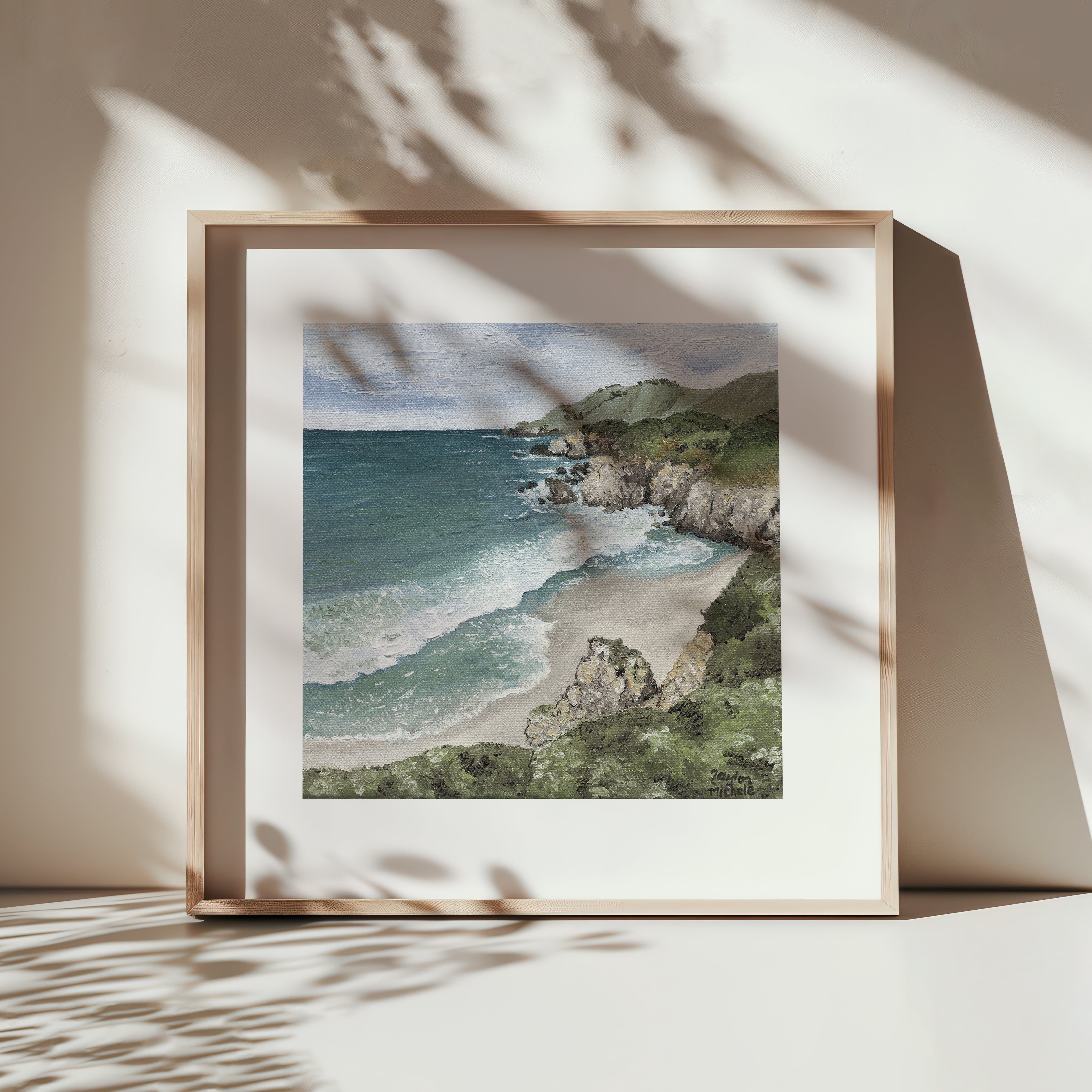 Framed artwork of a coastal landscape with a beach and ocean.