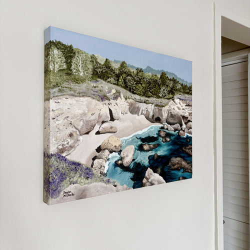 Canvas print of a landscape with rocks, water, and trees on a white wall.