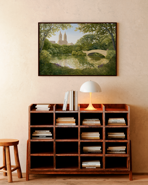 Framed artwork of a park scene above a wooden bookshelf with books.