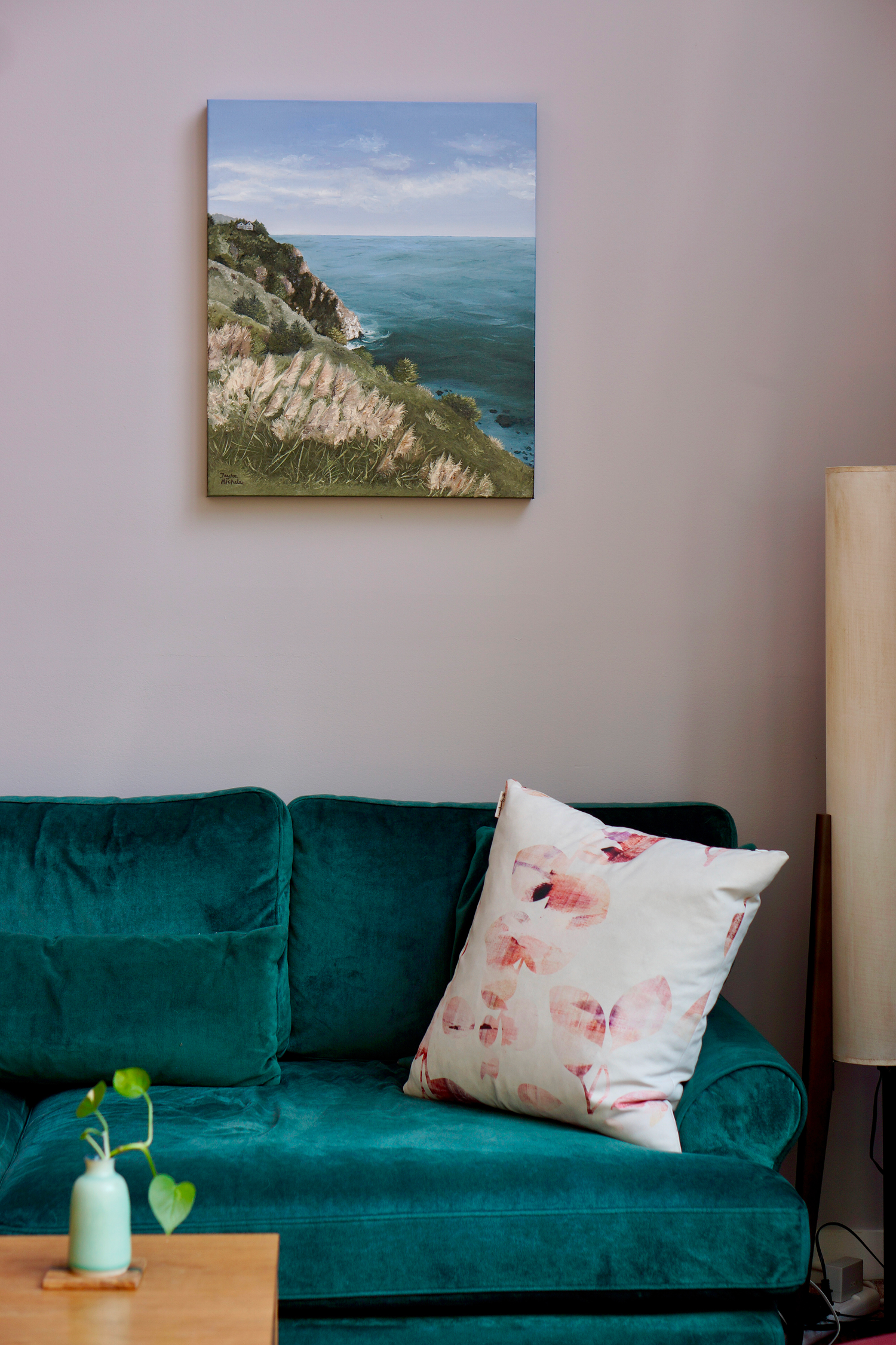 Teal sofa with a floral pillow in a room with a coastal painting on the wall.