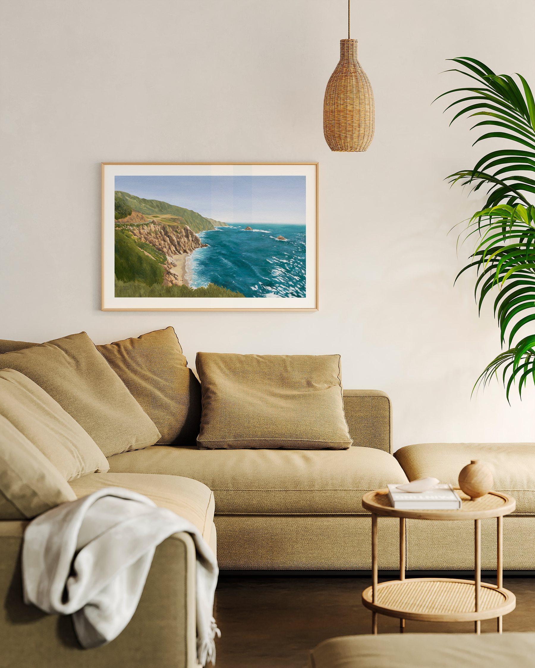 Framed coastal California landscape oil painting featuring dramatic ocean cliffs, turquoise blue water, and rugged shoreline inspired by the Pacific Coast Highway. Fine art print styled in a warm neutral living room, beige couch, small coffee table, with natural textures and woven pendant lighting.