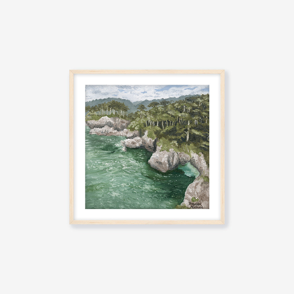 Framed fine art print of a coastal landscape with rocky cliffs and greenery. Maple frame