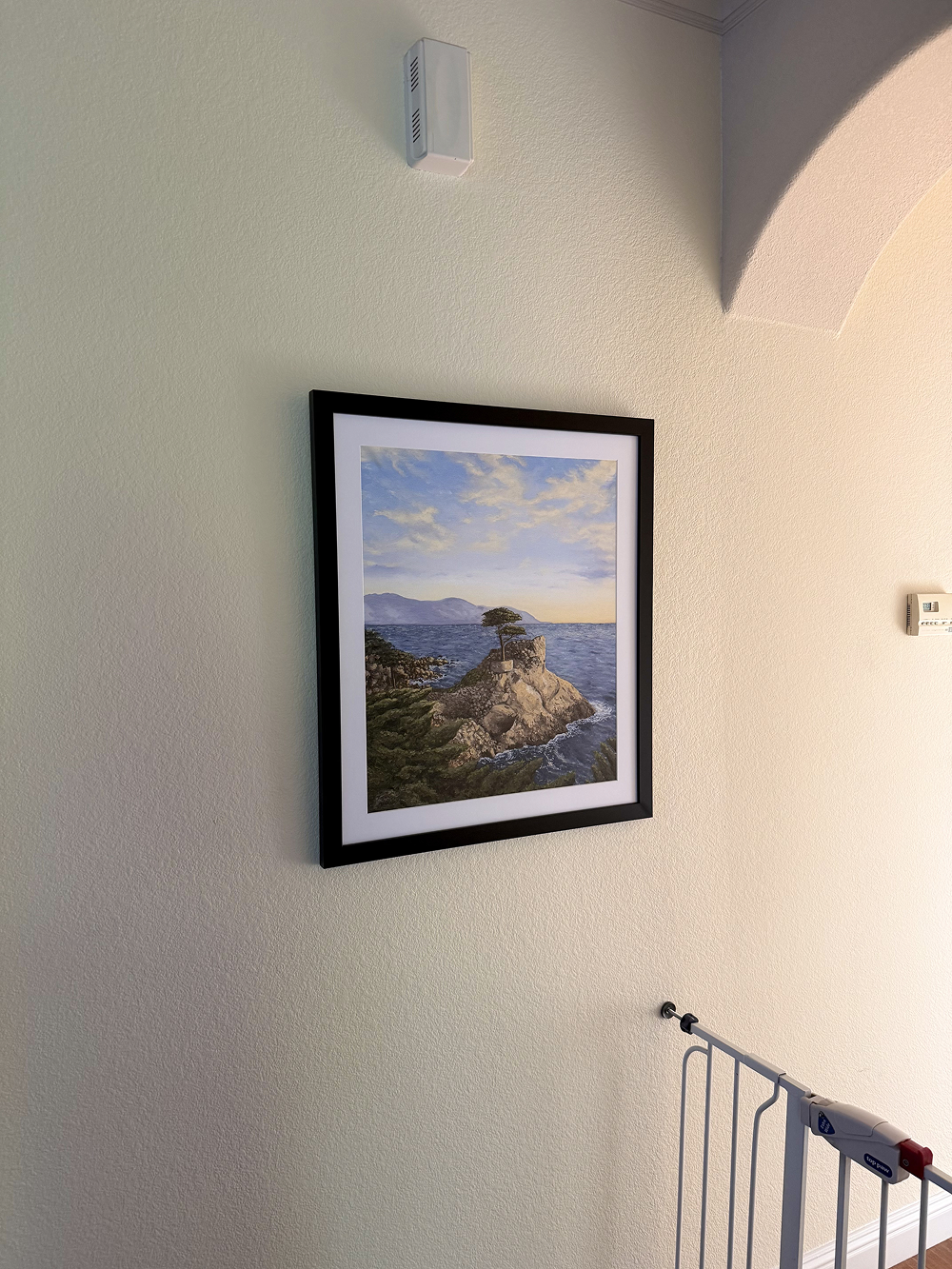 Framed artwork of a coastal scene on a wall next to a staircase.