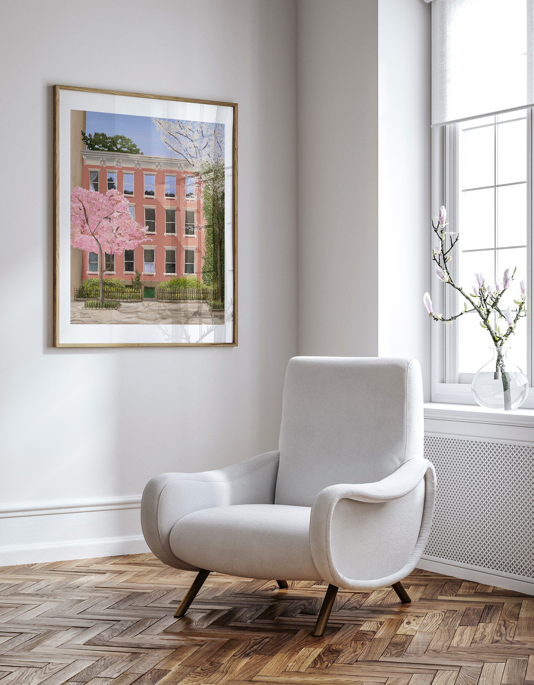 White armchair in a room with a framed picture of a salmon pink building  in the west village and cherry blossoms to the left and a vine on the right, hanging on the wall.