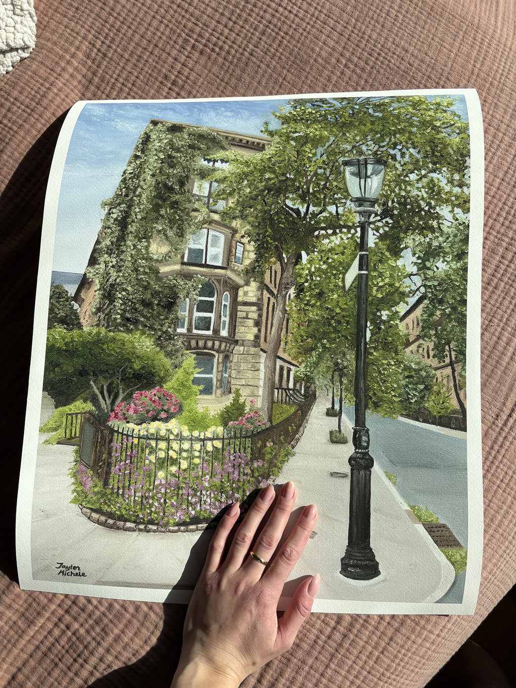 A woman's hand holds a 16 x 20" fine art print of the East Village New York City brownstone painting against an earthy pink background