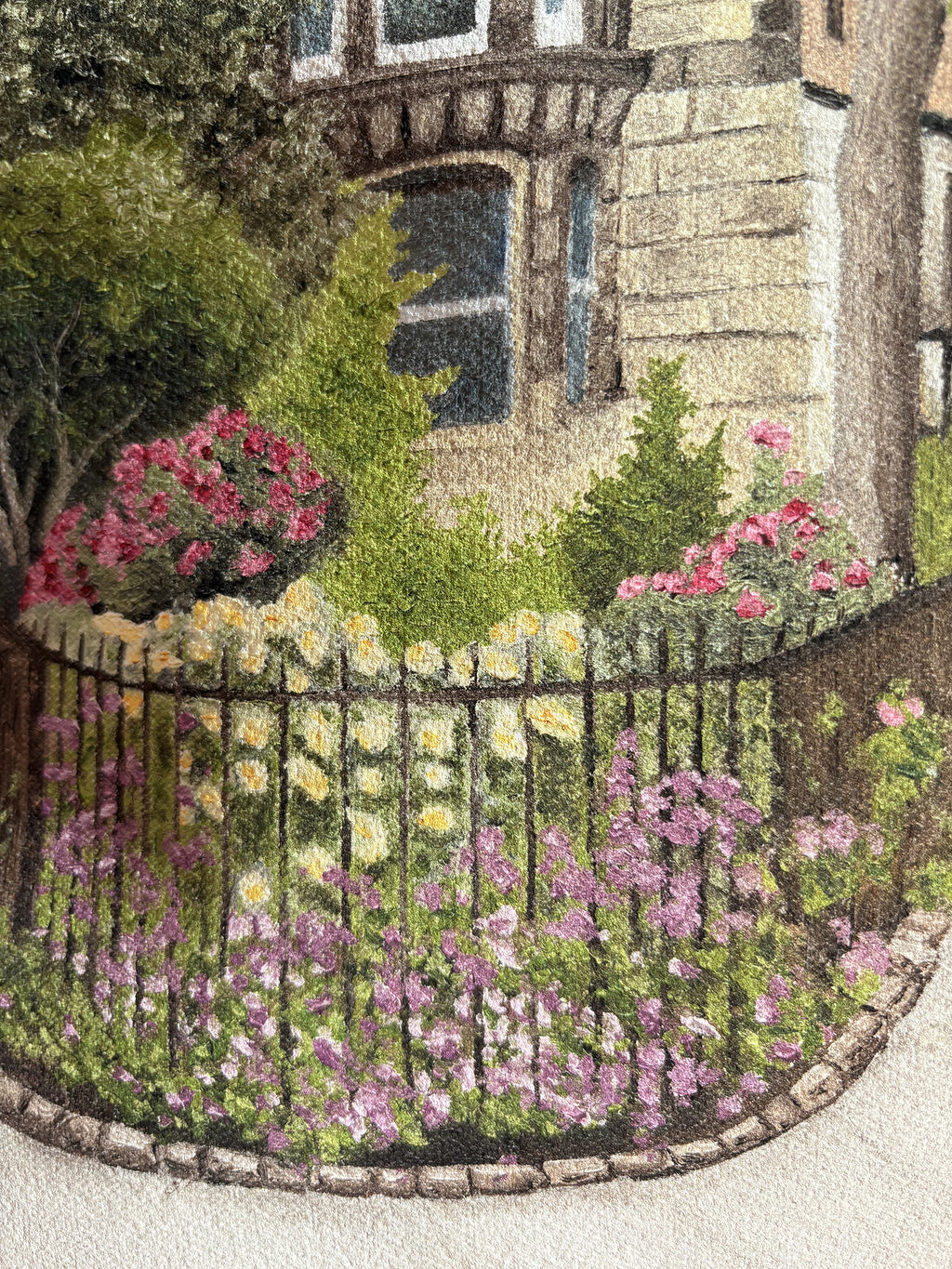Close up displaying the textured painting details of a fine art print of an East Village New York City street scene with a building, lamp post, and garden held by a hand on a textured brown surface.