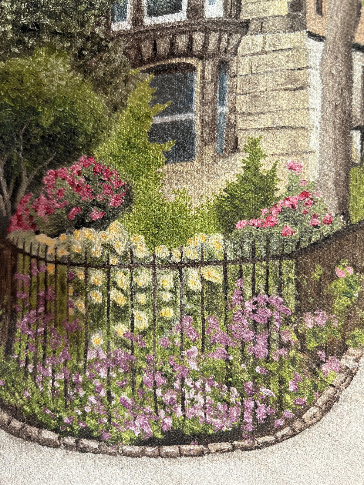 Close up displaying the textured painting details of a fine art print of an East Village New York City street scene with a building, lamp post, and garden held by a hand on a textured brown surface.