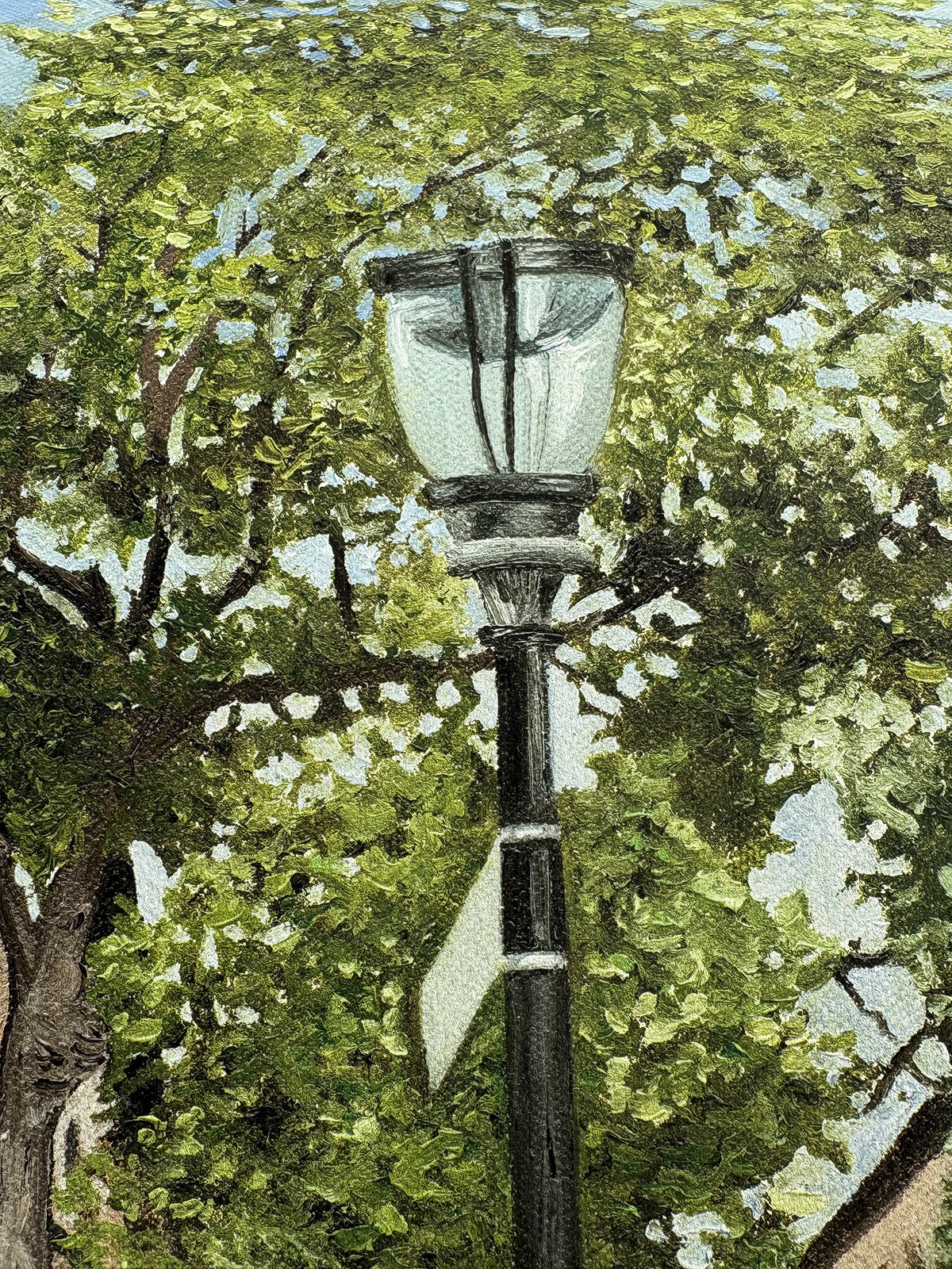Close up showing the painting details of the lamp post with leafy green trees in the background and little specks of blue sky in the distance. 