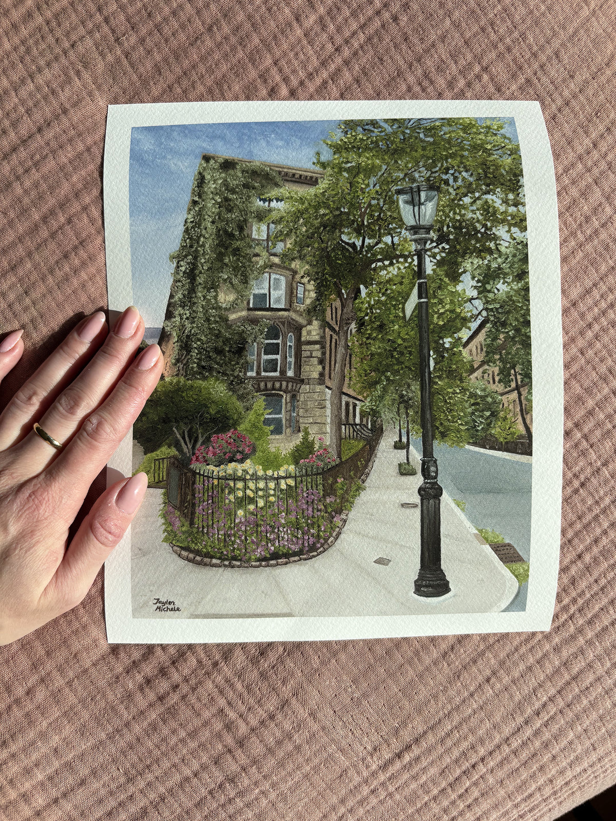 A woman's hand holds a 8x10" fine art print of the East Village New York City brownstone painting against an earthy pink background