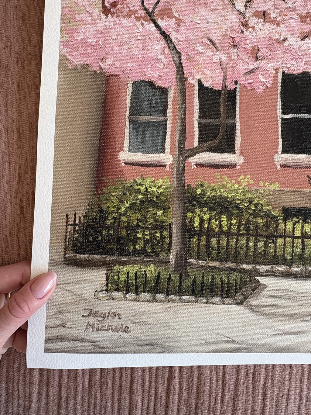 Painting of a cherry blossom tree in front of a red brick building, held by a hand.