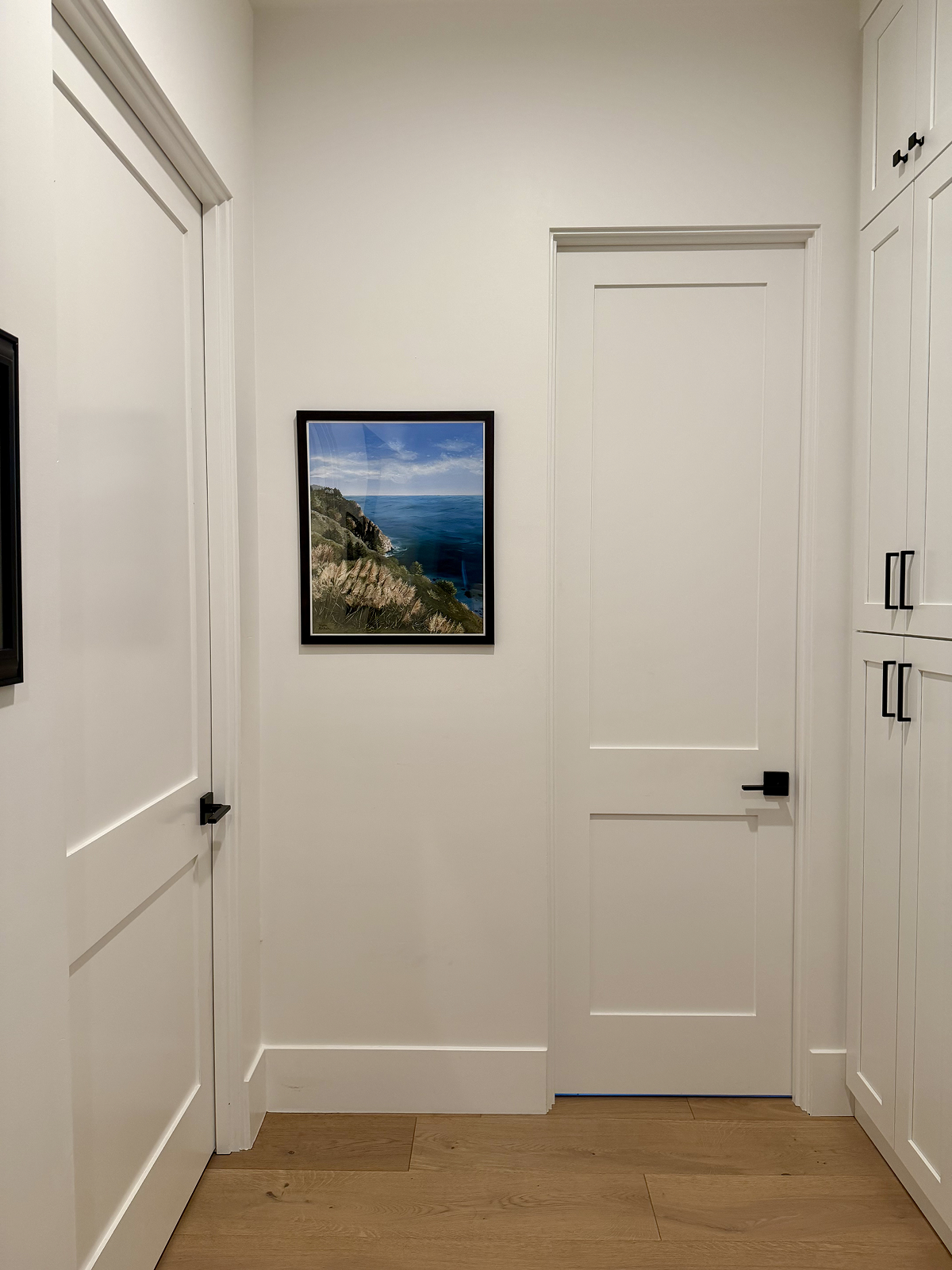 Foyer with white walls, doors, and a framed picture of a coastal scene.