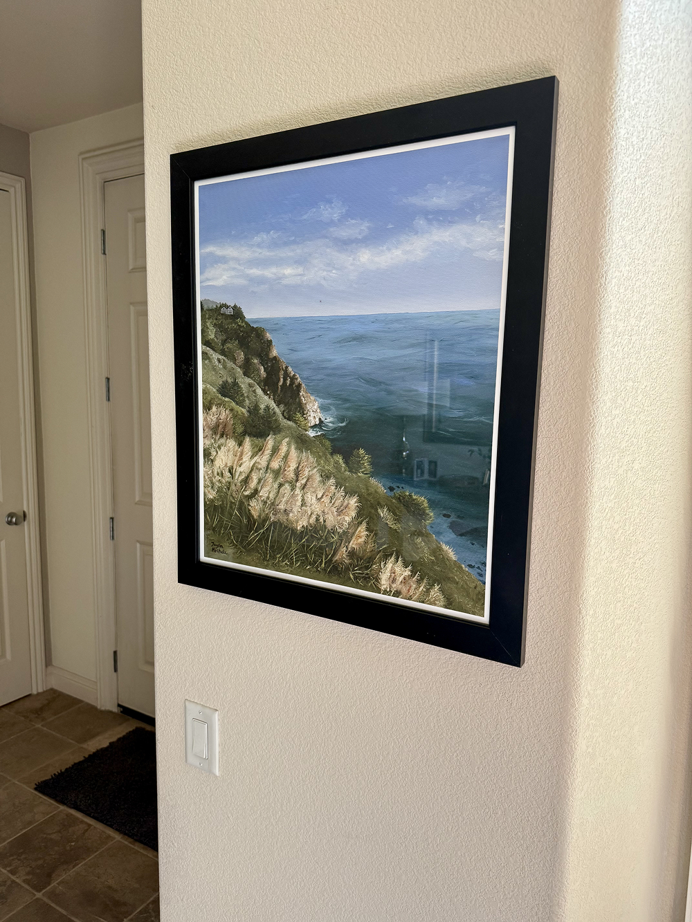 Framed artwork of a coastal scene on a beige wall.